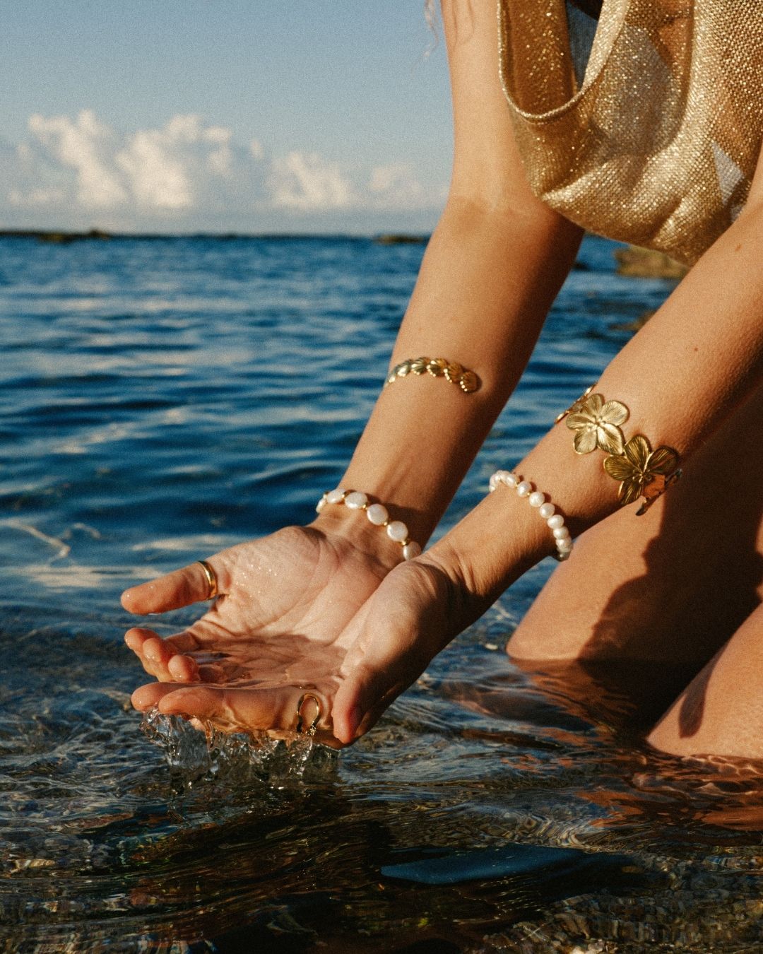 Person with gold bracelets and anklets touching water by the sea